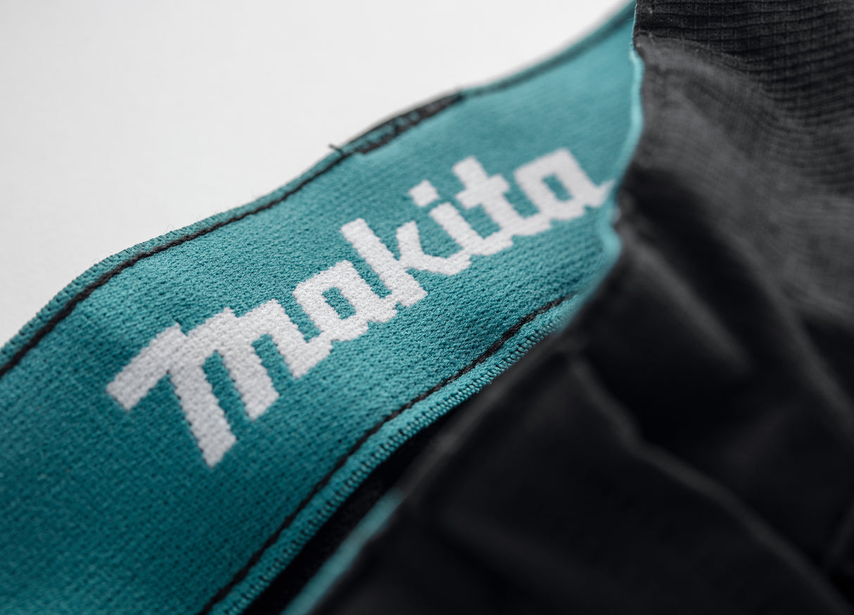 Close-up of a Black Makita Onyx 4 way stretch trousers with a teal waist banc and white Makita logo.