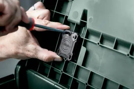Image showing the Metabo GPS Tracker being screwed into the lid of a metabo metaloc case. A hand can be seen holding the tracker, while a screwdriver is tightening the screws. It is being attached to a green metabo metaloc case.