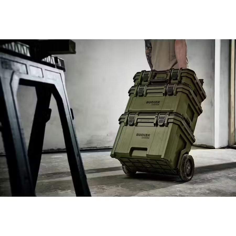 Person pushing a stack of green Bunker cases in an industrial setting
