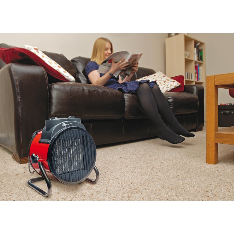 Person sitting on a couch reading a book with a space heater in the foreground