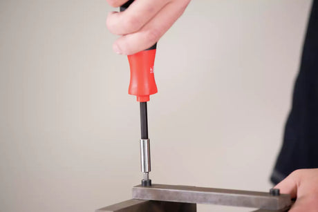 Person using a red-handled screwdriver on a metal surface with a plain background