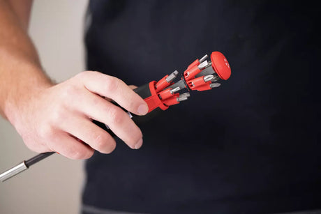 Person holding a red and black Wiha screwdriver with multiple components against a dark background
