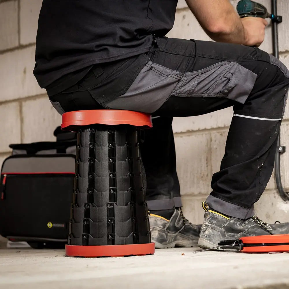 Avit Collapsible Stool AV00010 being sat on while a worker is attaching pipe clips to a wall.