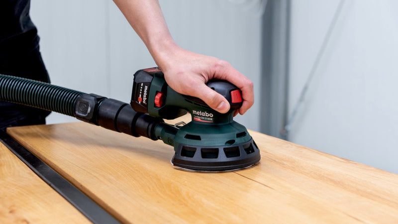 Person using a sanding machine on a wooden surface with a neutral background