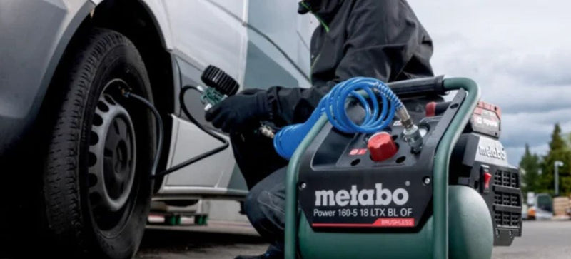 Person using a Metabo air compressor on a car tire outdoors.