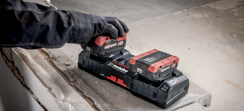 Person using a Metabo power tool battery charger on a concrete surface