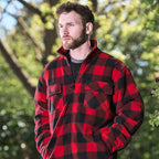 Man wearing a red and black checkered jacket outdoors with greenery in the background