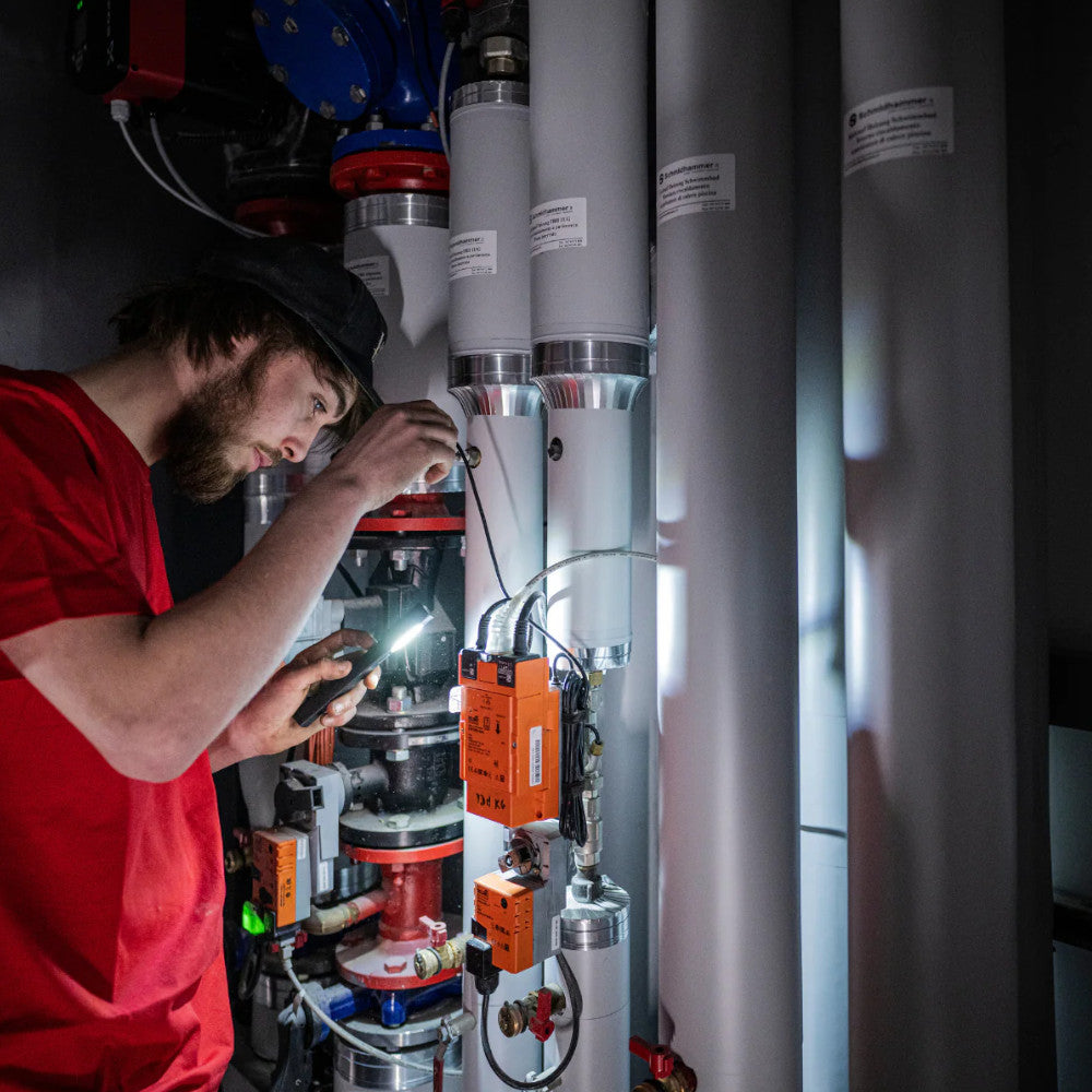 Person working on mechanical equipment with a flashlight in a dark setting