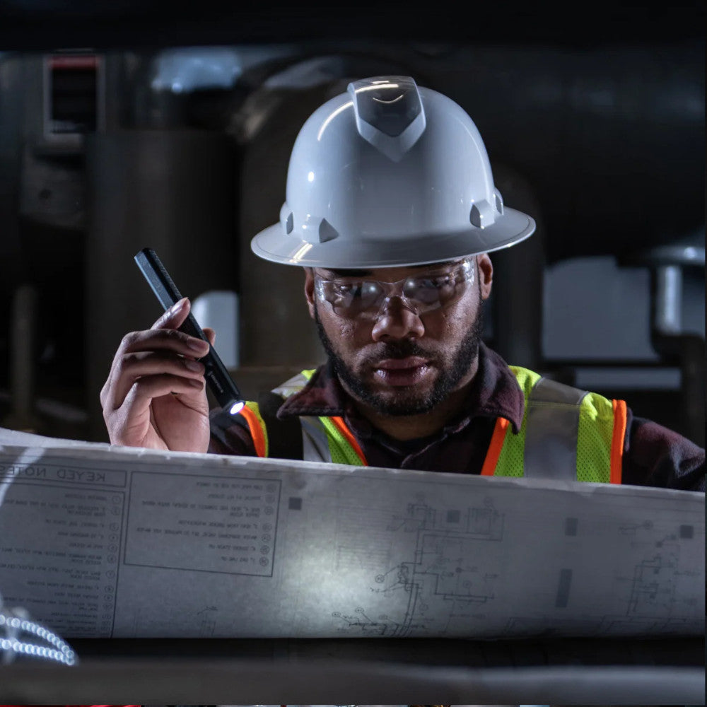 Construction worker in hard hat and safety glasses holding a Black Ledlenser WR2 Inspection pen light, looking at blueprints.