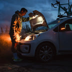 Person checking car engine at night with headlights on