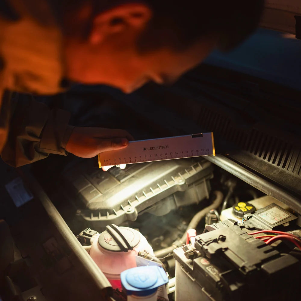 Person checking a car's engine with a flashlight.
