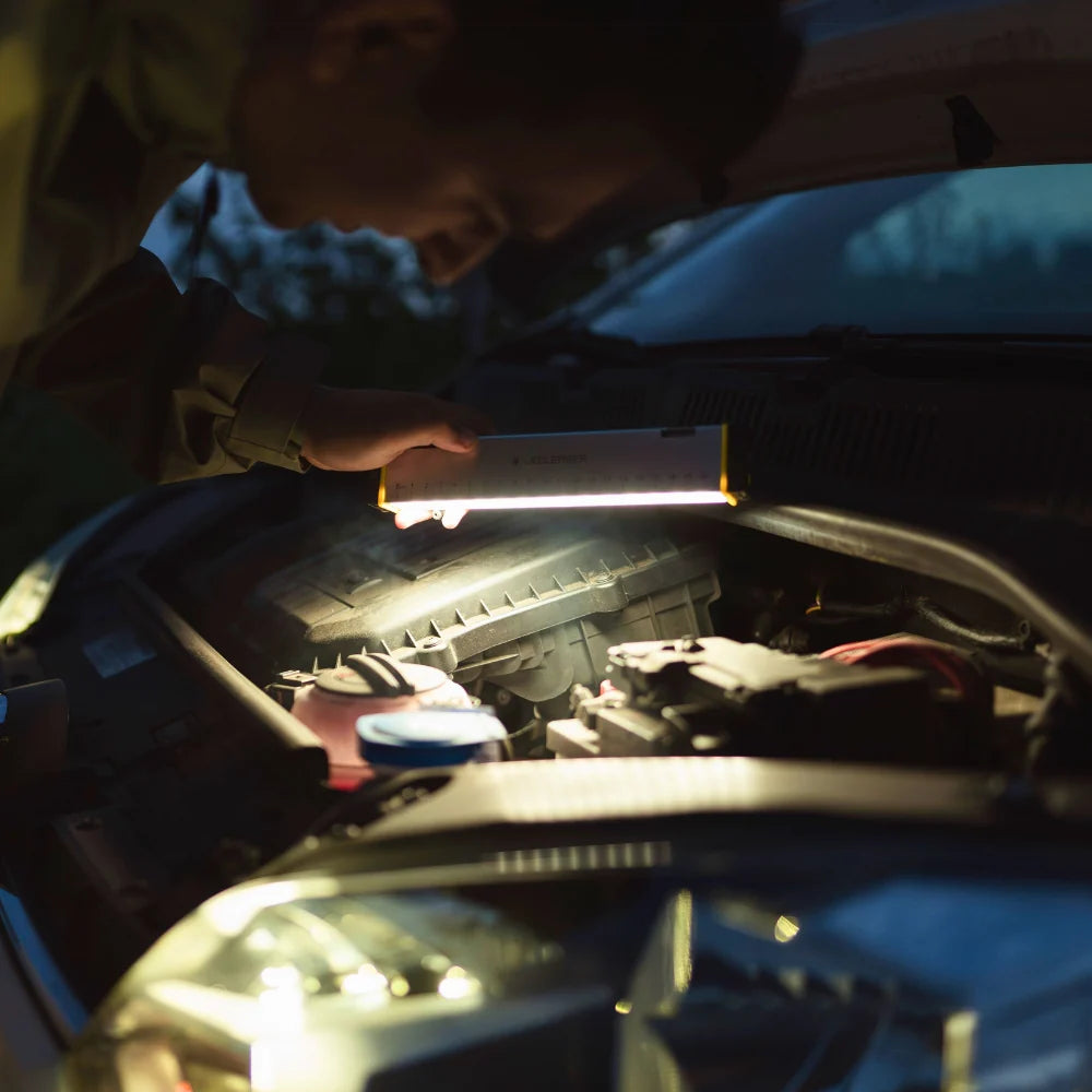 Person working on a car under the hood with a flashlight