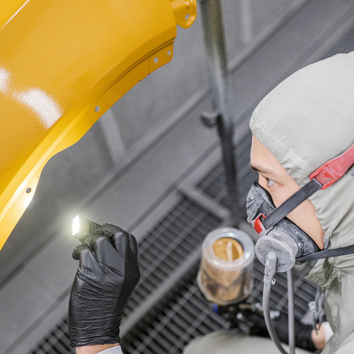 Person in a protective suit and mask using a flashlight on a yellow object.