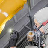 Person in a protective suit and mask using a flashlight on a yellow object.