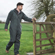 Man in a green coverall standing next to a wooden gate in a field
