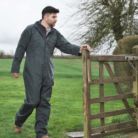 Man in a green coverall standing next to a wooden gate in a field