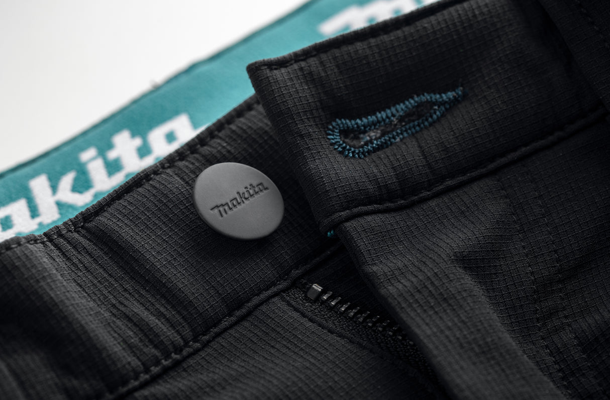 Close-up of the Black Makita Onyx 4 way stretch trousers showing a Makita button with logo on a white background