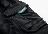 Close up of the pocket on the black Makita Onyx 4 way stretch trousers with a turquoise Makita label on a white background