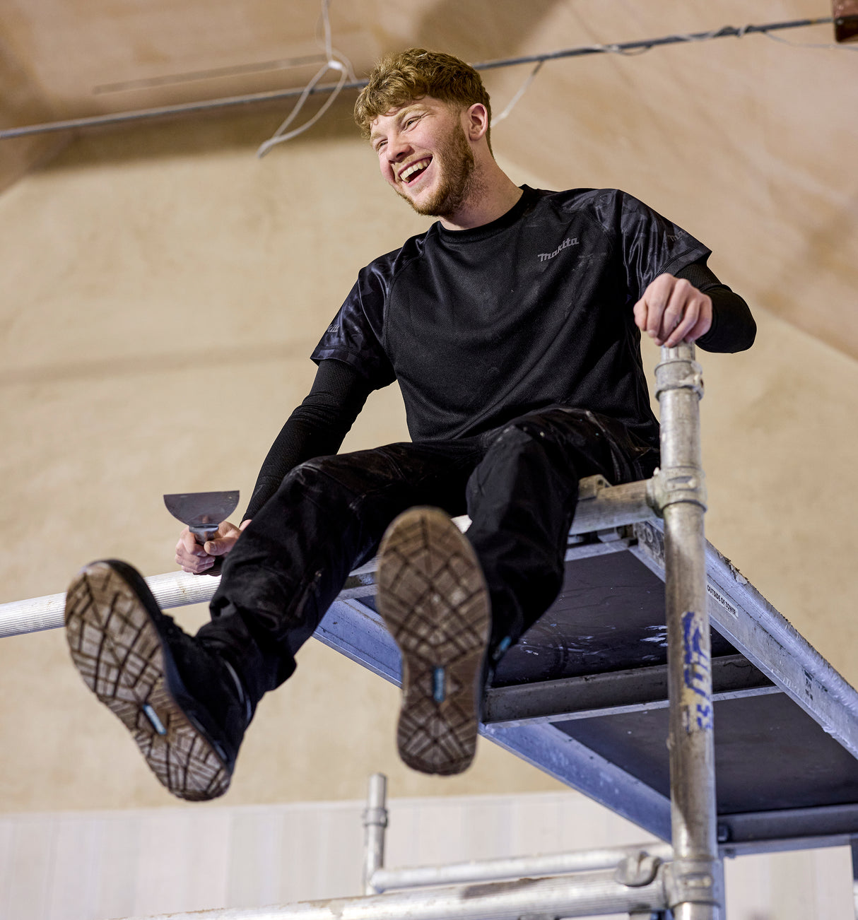 Man sitting on a metal structure wearing Makita workwear.