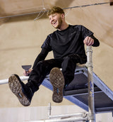 Man sitting on a metal structure wearing Makita workwear.