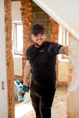 Man in a black Makita Tech t-shirt and Makita cap standing in a room under renovation with tools.