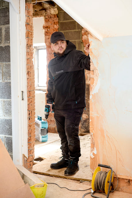 Person in Makita workwear holding a drill in a room under construction