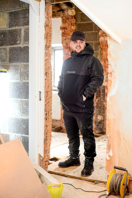 Person wearing Makita workwear with a Makita logo in a room under construction.