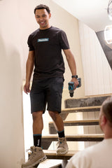 Man standing on stairs wearing Makita Axis Stretch Shorts in black and a black Makita t-shirt and holding a drill.