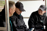 Three men wearing black jackets and Makita hats, sitting together on a vehicle.