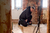 Person working on a renovation project in a room with exposed brick walls and wooden floor.