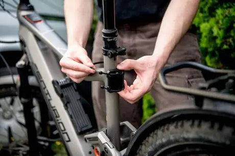 Image showing the Metabo GPS Tracker for iPhone being attached to the seat post of a silver / grey bicycle with cable ties to enable tracking of the bicycle. A person in brown trousers and a black top can be seen tightening the cable ties. 