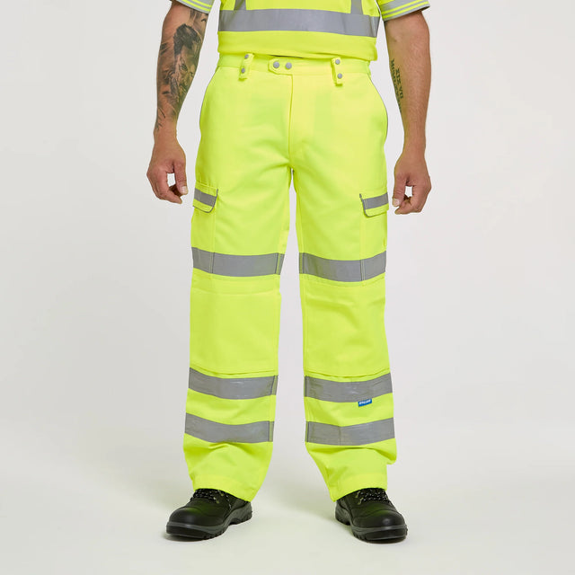 A model wearing high-visibility neon yellow cargo trousers with reflective silver stripes, shown from the waist down on a light gray studio background.