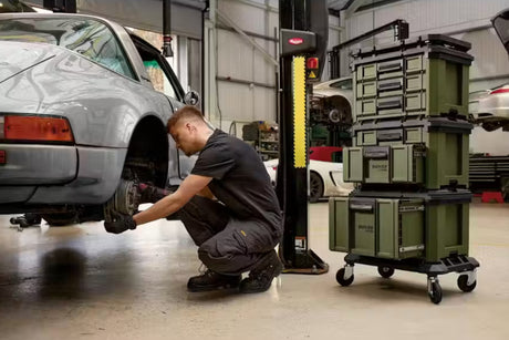 Mechanic working on a car in a garage with Bunker Load Up and equipment.
