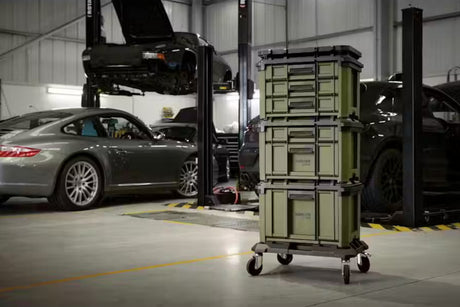 Stack of green Bunker load up containers on a cart in a warehouse setting with cars in the background.