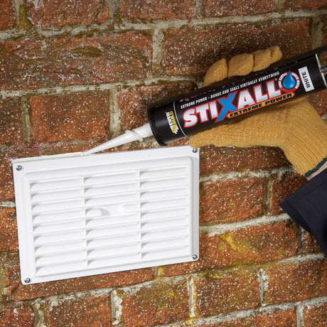 Person applying STIXALL sealant to a brick wall with a white vent.